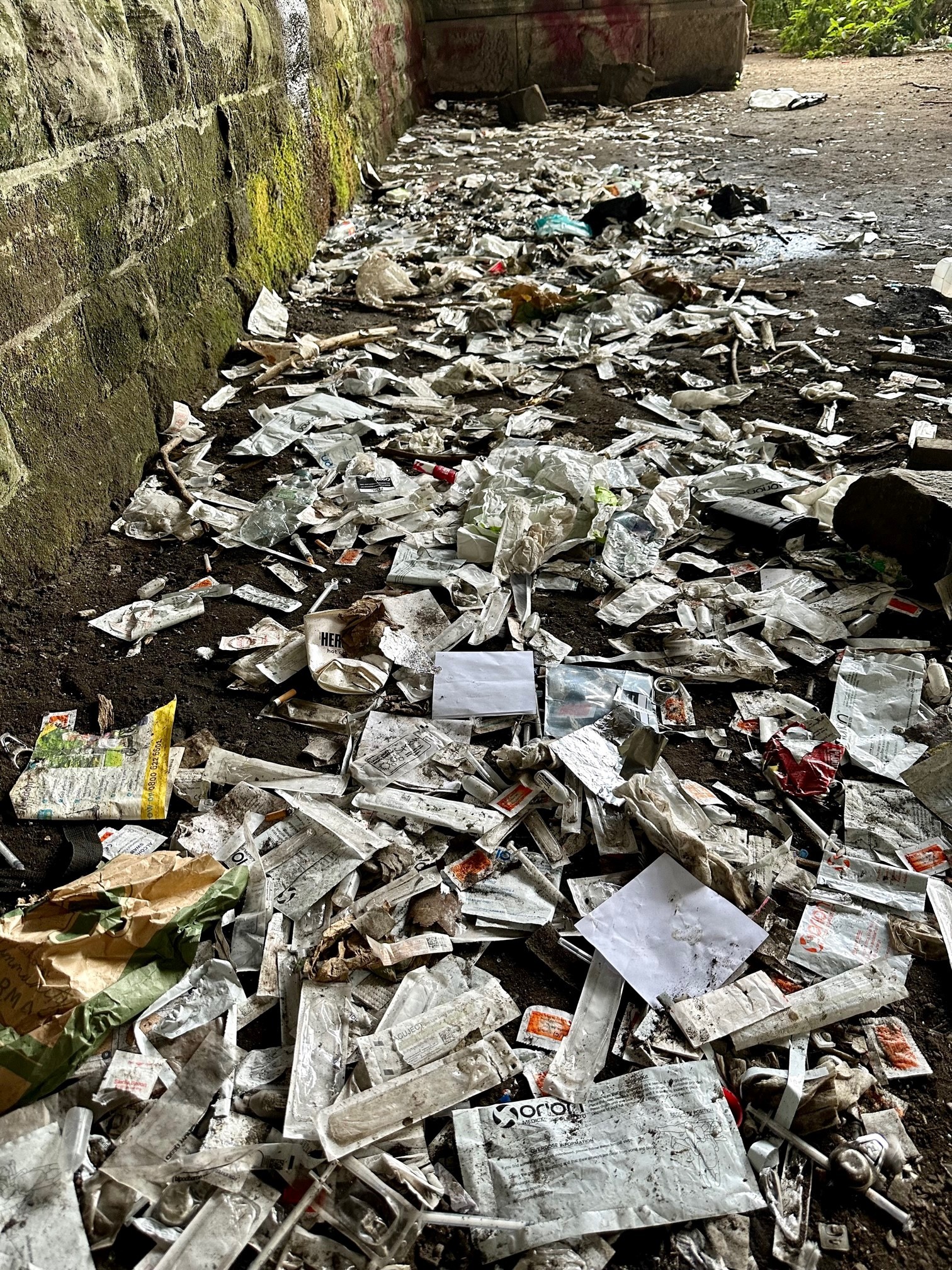 The floor of an alley strewn with discarded needles and other debris.