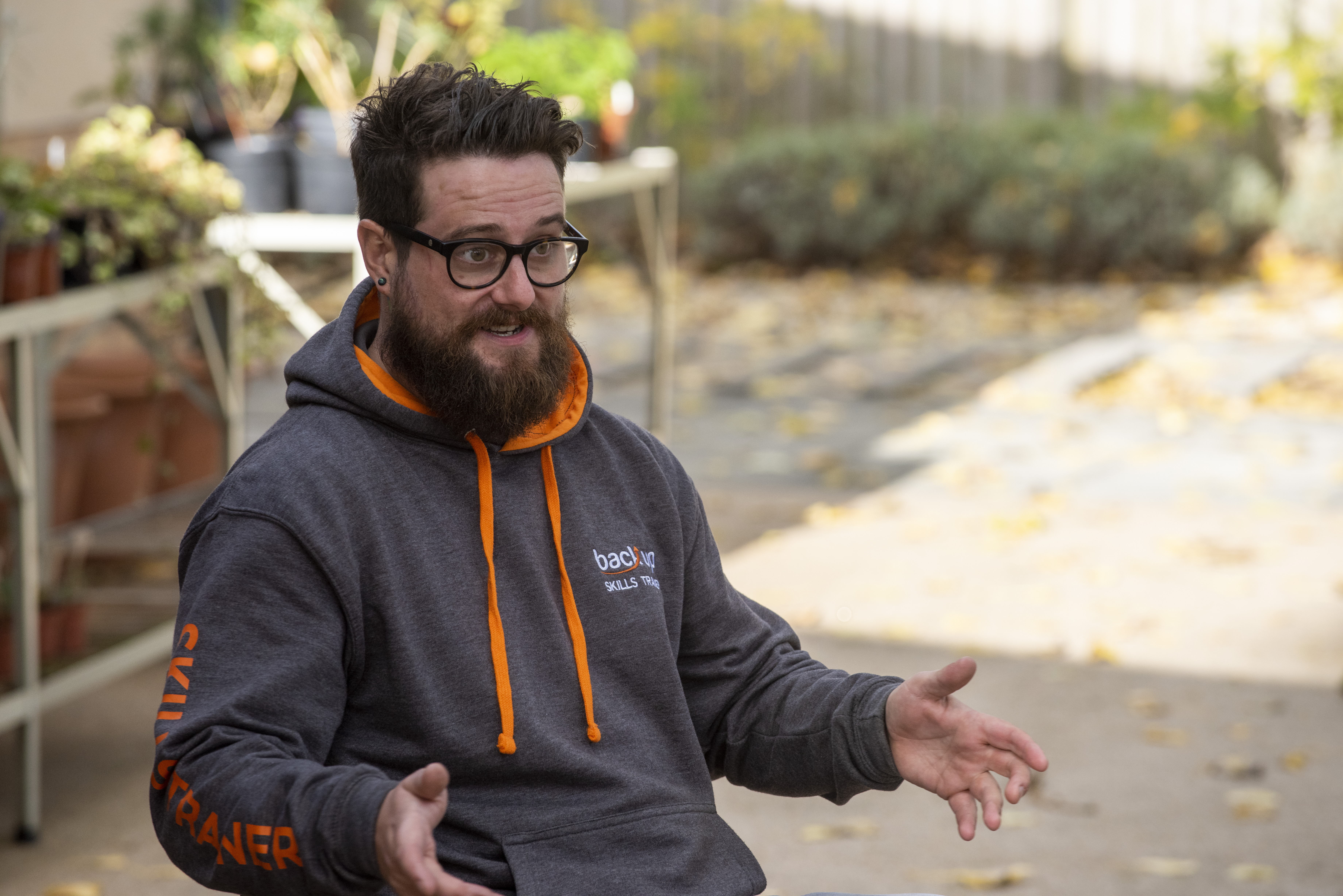 Photograph of a man with a beard and glasses wearing a grey and orange hoodie that says "Back up"